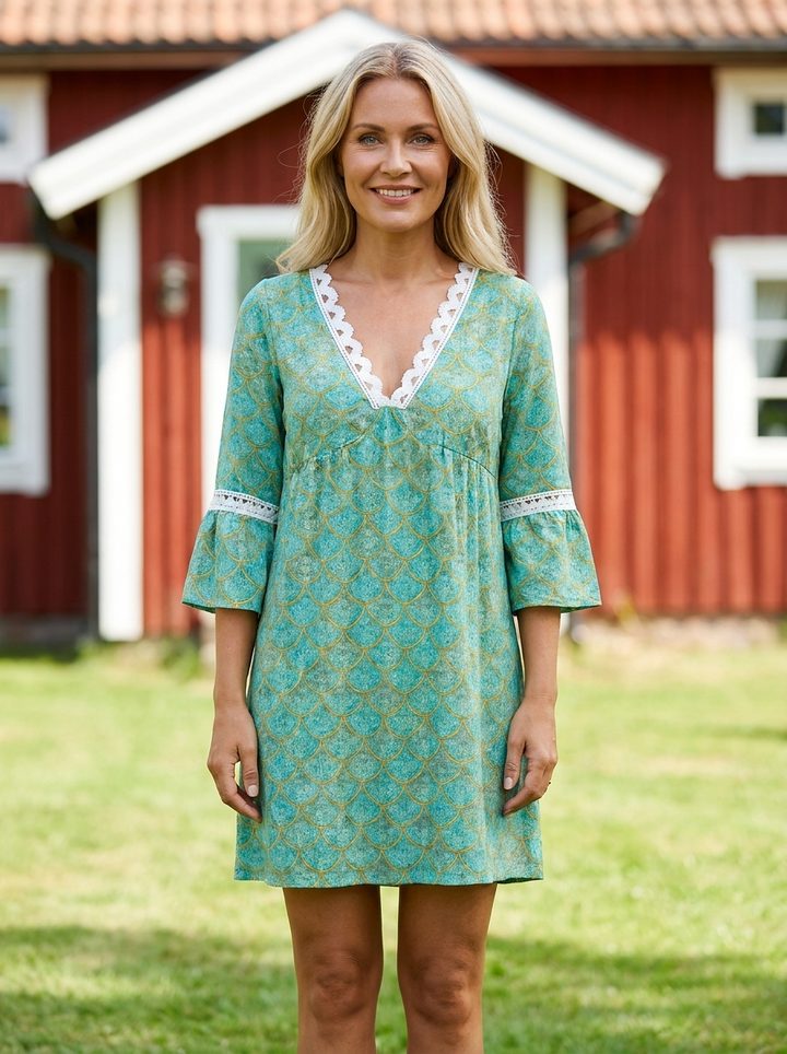 Alva knälång sommarklänning i turkosgrönt mönster med vit spetskant, buren framför rött sommarhus – lissendra.com